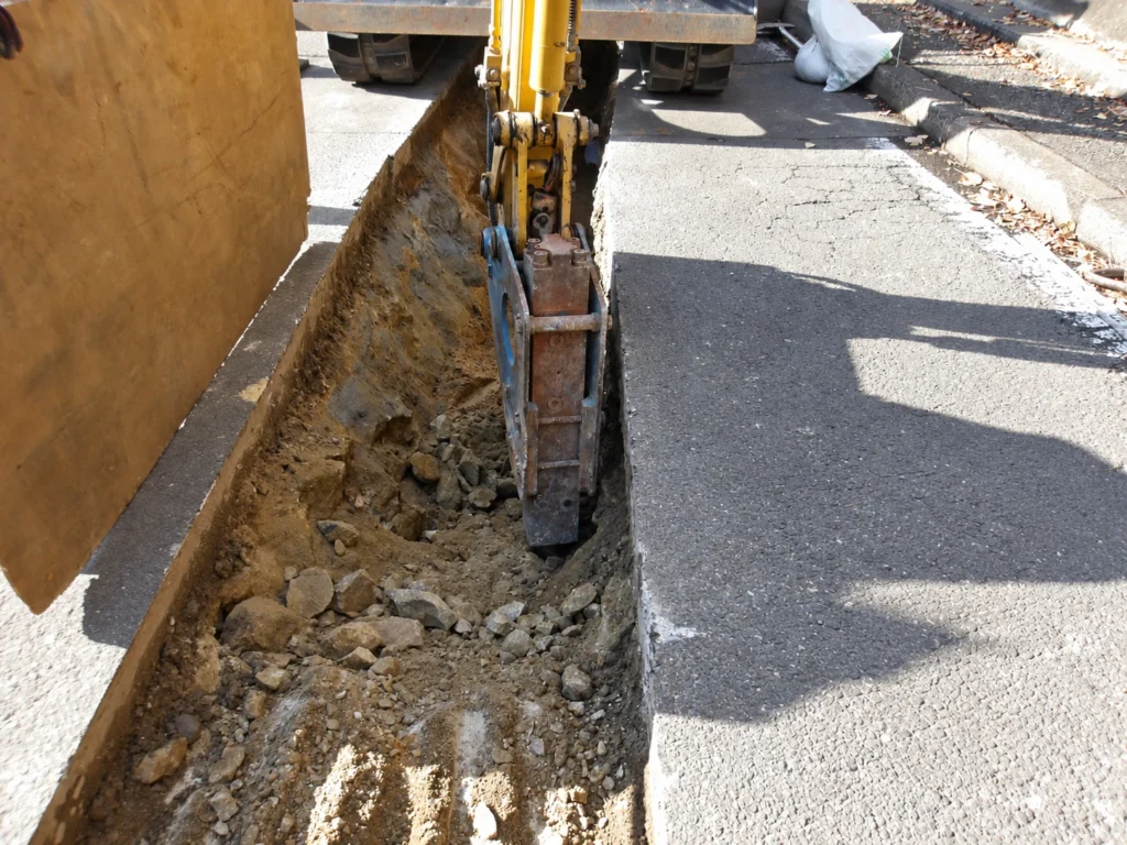 小榊線線路変更工事（管路工事）：管路用の掘削溝で、ブレーカーにより岩盤を破砕する作業