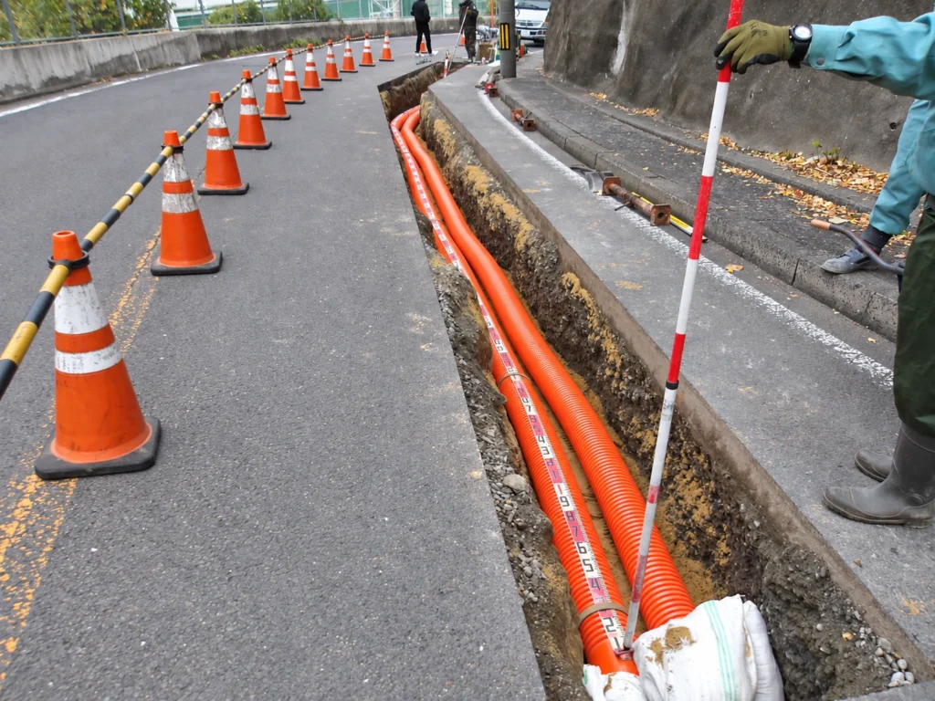 小榊線線路変更工事（管路工事）：道路沿いの溝に布設した管路と延長を確認する測定器具