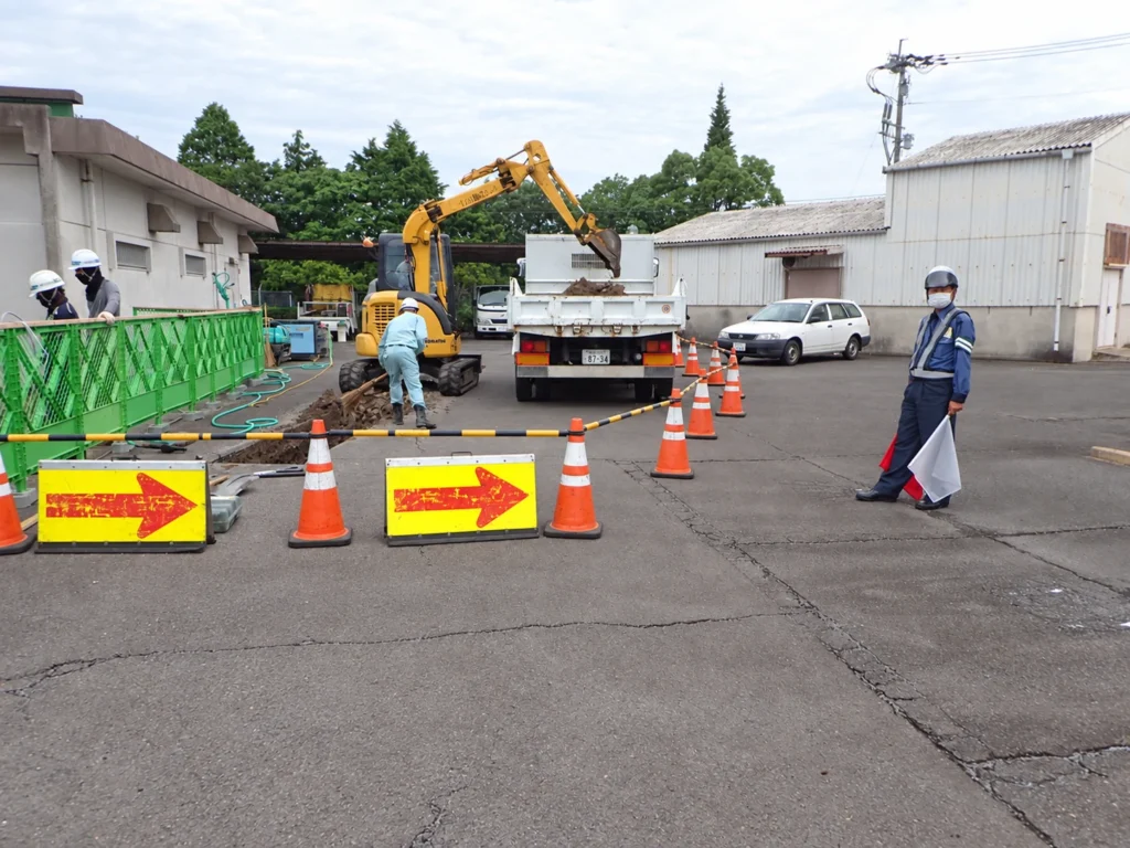 九州エア・ウォーター供給工事：カラーコーンとバリケードで作業区域を区画し、車両誘導を行う現場