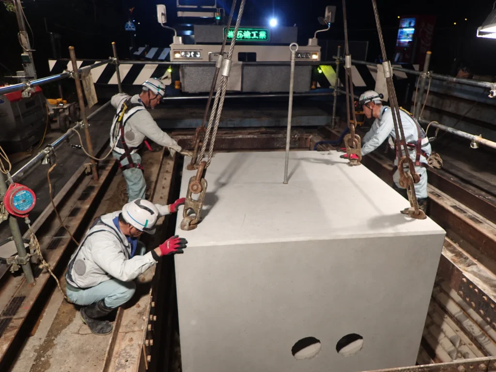 九州エア・ウォーター供給工事：夜間にプレキャストマンホール（A-Ⅰ形）を吊り込み据え付ける作業