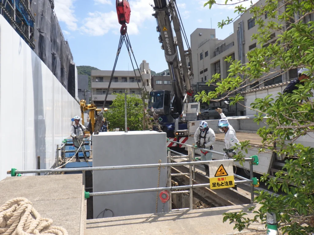 長崎スタジアムシティ供給工事(MH据付):作業員が合図・位置確認を行いながら、マンホールを据え付ける作業