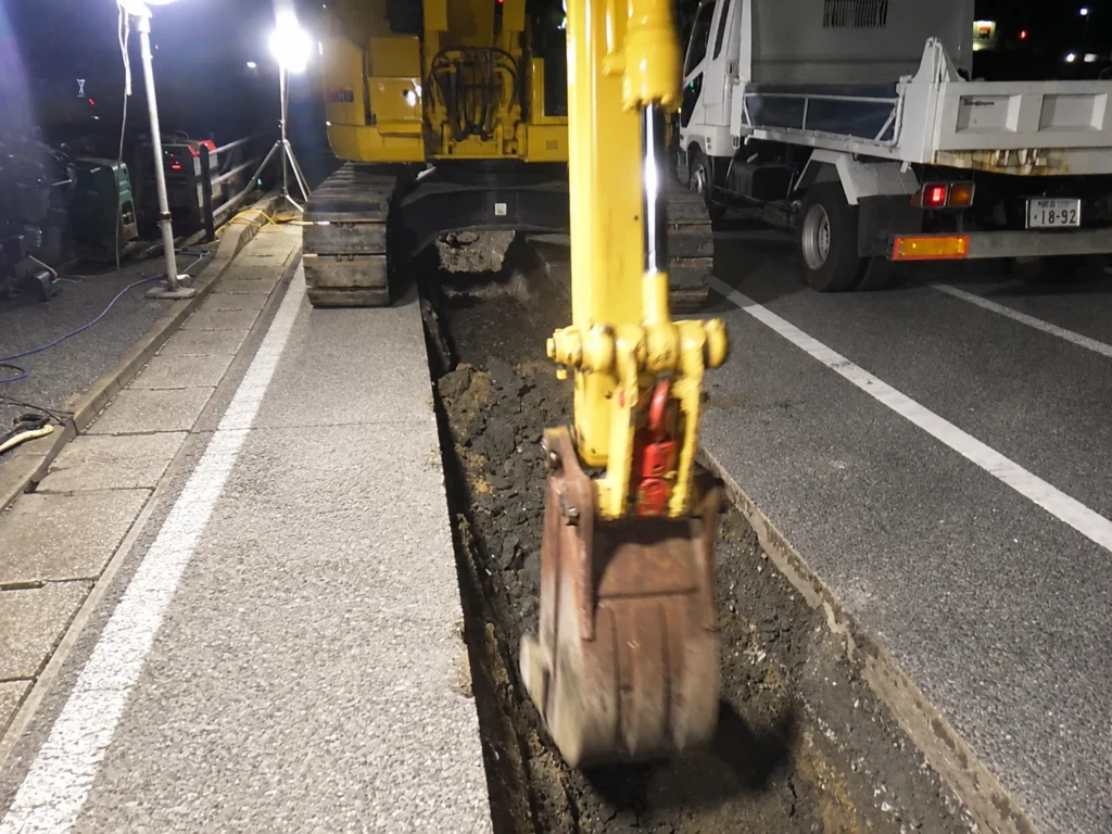 長崎スタジアムシティ供給工事(MH据付):作業灯を設置して行う、夜間の管路部掘削