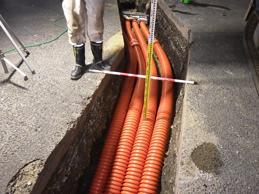 掘削溝に敷設した電線用の管路と、敷設状況を確認する測定器具