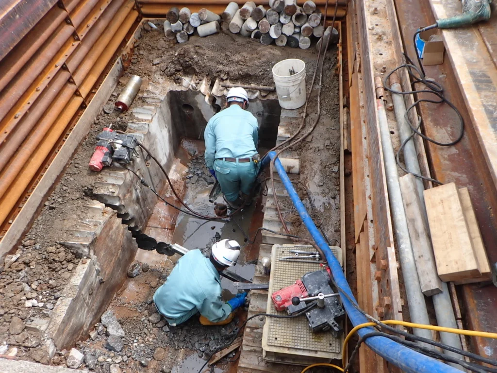 長崎駅周辺土地区画整理事業（2工区）電線共同溝工事：既設マンホールの撤去に向けて削孔を行う作業
