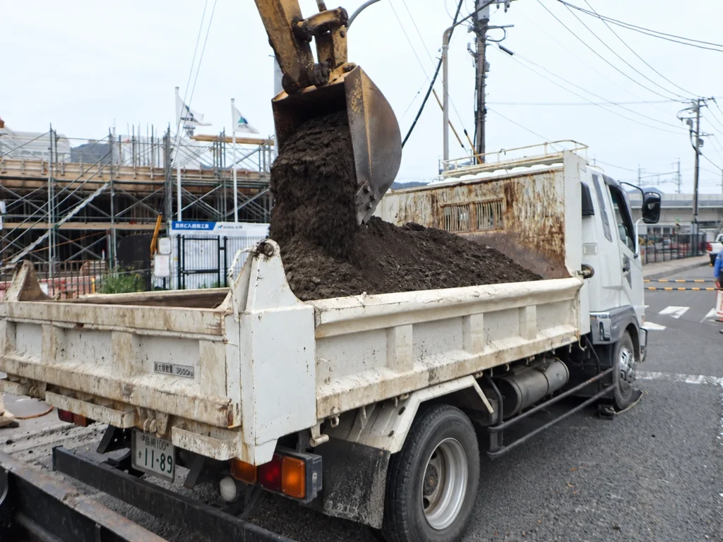 長崎駅周辺土地区画整理事業（2工区）電線共同溝工事：残土をバックホウでダンプへ積み込む作業